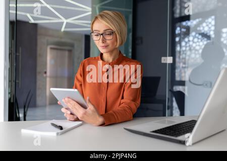 Porträt einer erfolgreichen und fokussierten jungen Designerin. Ein Ingenieur, ein Architekt, der mit einem Tablet arbeitet. Im Büro am Tisch mit einem Laptop sitzen. Stockfoto