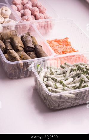 Behälter mit gefrorenem Gemüse und halbfertigen Fleischprodukten aus dem Kühlschrank. Fleischbällchen, Knödel, Dolma in Traubenblättern, gehackte Bohnen Stockfoto