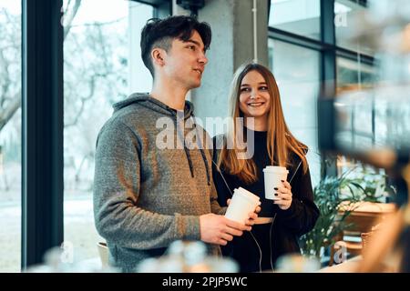 Freunde, die in einem Café einkaufen. Junge Männer und Frauen plaudern, während sie beim Zählen Gebäck, Backwaren und heiße Getränke pflücken Stockfoto