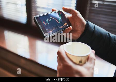 Person, die den Handel auf dem Aktienmarkt für Kryptowährungen mithilfe der Anwendung für Investitionen auf dem Smartphone investiert. Aktienmarktinvestitionen in der Hand. Händler, der Mob hält Stockfoto