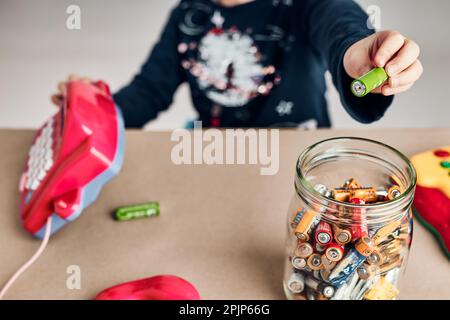 Kleines Mädchen, das gebrauchte Batterien zum Recycling in den Becher legte. Kinder trennen Abfall. Behälter nur für Batterien Stockfoto