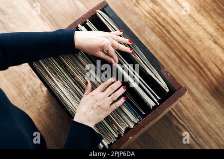 Vinyl-Schallplatten spielen. Musik von einem Vinyl-Plattenspieler hören. Retro- und Vintage-Musikstil. Frau mit analogem LP-Plattenalbum. Stapel alt Stockfoto