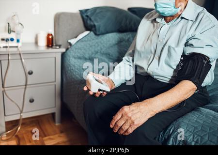 Leitender Mann, der den Blutdruck und die Herzfrequenz selbst misst. Überprüfung des Gesundheitszustands älterer Patient, der an arterieller Hypertonie leidet Stockfoto