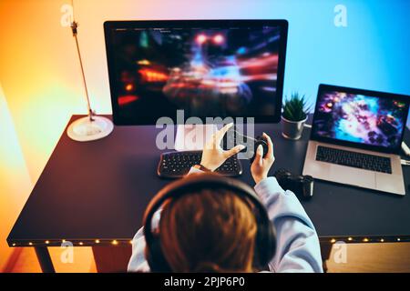 Teenager Mädchen spielen Videospiel zu Hause. Gamer mit Gamepads vor dem Bildschirm. Streamer spielt online in einem dunklen Raum, der von Neonlichtern beleuchtet wird. Stockfoto