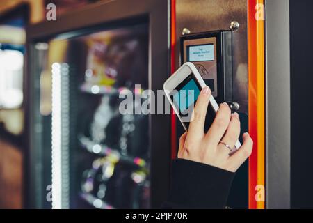 Frau, die für das Produkt am Verkaufsautomaten mit kontaktloser Zahlungsmethode mit dem Mobiltelefon bezahlt. Frau nutzt neue Zahlungsmittel Stockfoto