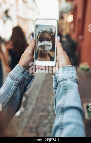 Junge Frau mit Videoanruf während des Spaziergangs in der Innenstadt chatting mit einem Freund trägt die Gesichtsmaske, um Virusinfektion zu vermeiden und zu verhindern, dass die SP Stockfoto