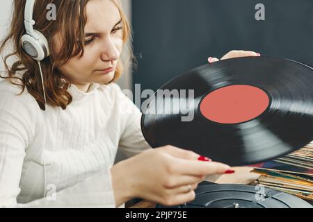 Junge Frau, die Musik von einem Plattenspieler hört. Wiedergabe von Musik auf Plattenspielern. Frau, die zu Hause Musik aus der alten Plattensammlung genießt. Stockfoto