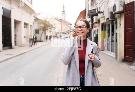Eine Frau mit Brille, die auf der Straße der Stadt auf dem Handy anruft. Stockfoto