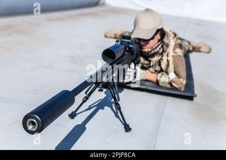 Scharfschützenmädchen zielte auf ihre Waffe, gekleidet in Tarnkleidung. Präzision, Geschick und Tapferkeit einer Schützin Stockfoto