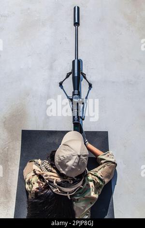 Scharfschützenmädchen zielte auf ihre Waffe, gekleidet in Tarnkleidung. Präzision, Geschick und Tapferkeit einer Schützin Stockfoto