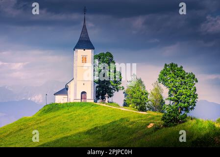 Jamnik, Slowenien. Die Jamnik Church ist eine malerische Kirche aus dem 15. Jahrhundert, bekannt für ihr unverwechselbares rotes Ziegeldach und die atemberaubende Aussicht auf die Berge. Stockfoto