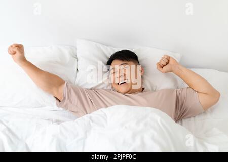 Draufsicht eines lächelnden Asiaten, der sich im Bett streckt Stockfoto