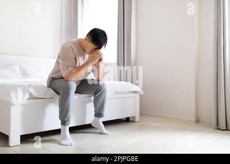 Unglücklicher erwachsener asiatischer Mann, der zu Hause im Bett sitzt Stockfoto