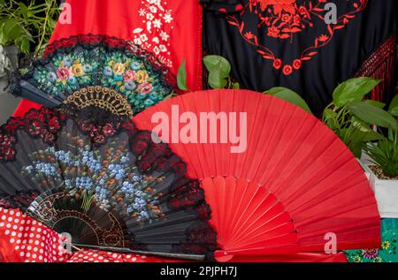 Nahaufnahmen-Fans in verschiedenen Farben, rot und schwarz mit Blumen und Spitzen und Schals im Hintergrund, typisch Andalusien. April-Messe Stockfoto