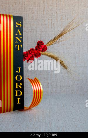 Sant Jordi, eine keramische Figur auf einem Buch mit schwarzem Einband, eine rote Papierrose, ein Buch mit einem leeren Blatt mit einem Band der katalanischen Flagge Stockfoto