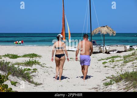 Ein Paar, das den Sandstrand entlang vor den Katamaran-Segelbooten spaziert. Familienurlaub an der tropischen Küste Stockfoto