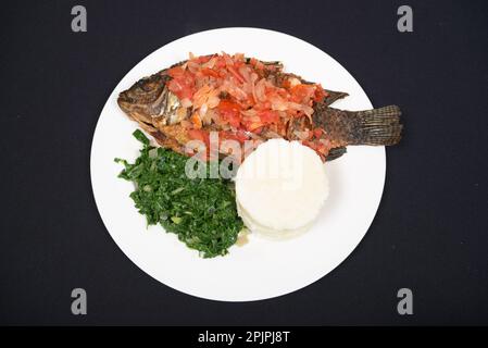 Gegrillter Fisch serviert mit Ugali und Gemüse auf abgelegenem Hintergrund Stockfoto