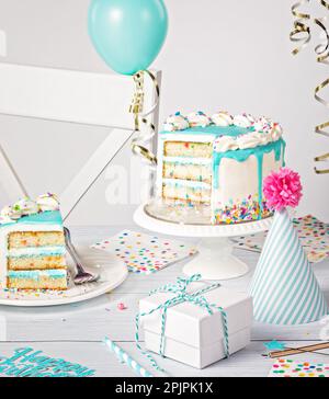 Geburtstagsparty mit blauer Ganache-Tropfenkuchen auf hellgrauem weißem Hintergrund mit Kuchenstückchen und Dekorationen. Stockfoto
