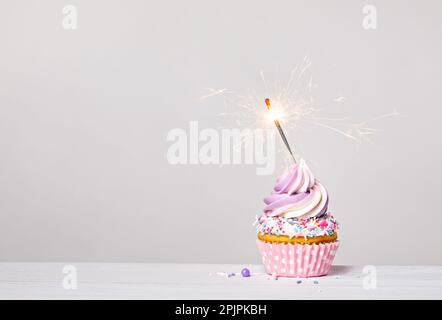 Lila und pinkfarbener Geburtstagscupcake mit Buttercreme-Glasur, Streuseln und beleuchtetem Glitzer auf hellgrauem weißem Hintergrund. Speicherplatz kopieren. Stockfoto