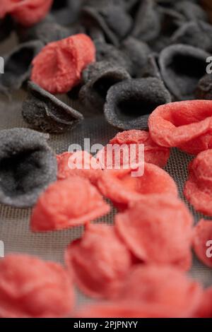 Eine Nahaufnahme von Orekchiette-Pasta in Schwarz und Rot auf weißem Hintergrund Stockfoto