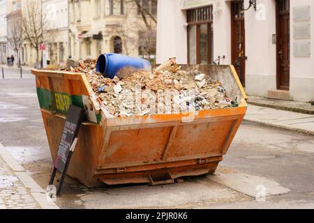 Der gelbe Metallbehälter ist mit Bauschutt gefüllt und kann von der Straße abgeholt werden. Stockfoto