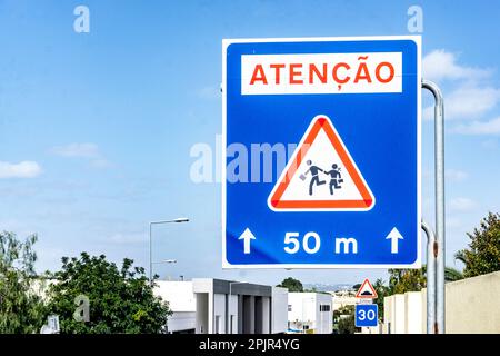 Ein portugiesisches Verkehrszeichen, das darauf hinweist, dass Kinder die Straße überqueren, Schule in der Nähe. Stockfoto