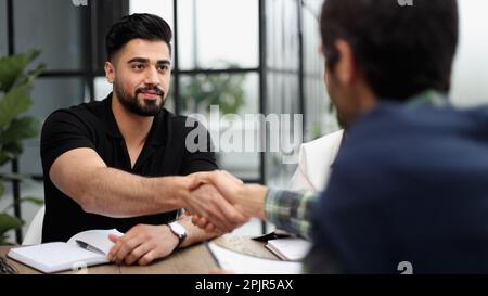 Willkommen an Bord. Eine Gruppe Geschäftsleute, die zwei Männer sitzen und sich die Hand schütteln Stockfoto