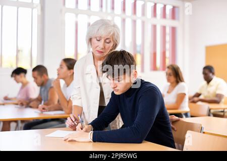 Alte Lehrerin, die dem Jungen hilft, Probleme im Unterricht zu lösen Stockfoto