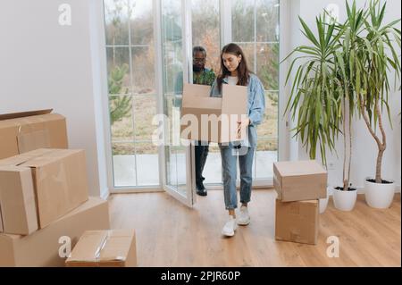 Ein junges Paar zieht in ein neues Haus. Ein afroamerikanischer Mann und seine Frau tragen Kisten in ein neues Haus. Eine Familie in einem neuen Haus Stockfoto