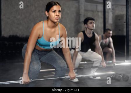 Energiegeladene junge Sportlerin, die Sit-ups mit Stange in der Nähe des Fitnessstudios anderer Leute übt Stockfoto