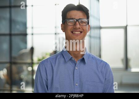 Nahaufnahme eines lächelnden asiatischen Geschäftsmanns, der in einem modernen Büro steht Stockfoto