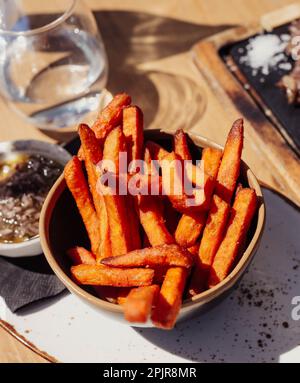 Pommes frites, serviert in einer Schüssel auf einem Holztisch. Süßkartoffeln Stockfoto