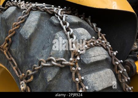Großer schwarzer Traktorreifen aus Gummi mit befestigten Stahlketten. Stockfoto