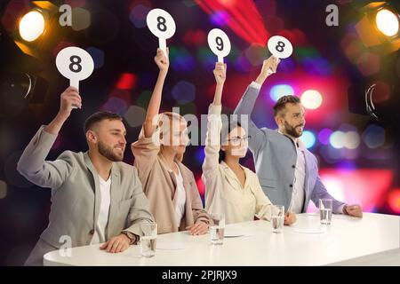 Jury-Gruppe mit unterschiedlichen Punktezeichen am Tisch vor verschwommenem Hintergrund. Bokeh-Effekt Stockfoto