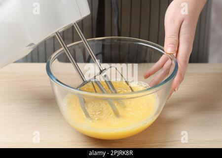 Eine Frau, die Eier mit einem Mixer am Holztisch schlägt, Nahaufnahme Stockfoto