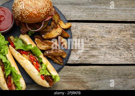 Leckere Burger, Hot Dogs, Kartoffelspalten und Soße auf einem Holztisch, Blick von oben mit Platz für Text. Fastfood Stockfoto