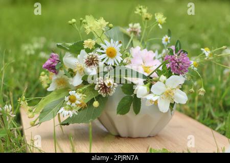 Keramikmörtel mit verschiedenen Wildblumen und Kräutern auf Holzbrettern auf der Wiese Stockfoto