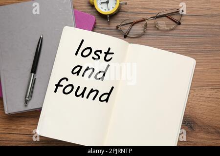 Notizbuch mit dem Satz Lost and Found, Stift, Brille und Wecker auf Holztisch, flach liegend Stockfoto