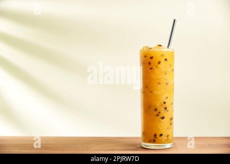 Glas eines erfrischenden Passionsfruchtsafts, Säfts oder Cocktails mit einem wiederverwendbaren ökologischen Strohhalm auf einer Holzfläche. Der Schatten eines tropischen Blatts ist p Stockfoto