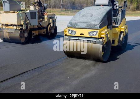 Arbeiter, der mit einer Vibrationswalzenverdichter-Prozessmaschine arbeitet und neuen Asphalt auf der Baustelle verlegt Stockfoto