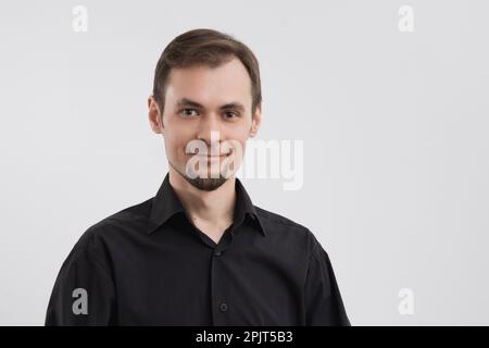 Ein weißer, ruhiger, lächelnder Mann 30s in einem schwarzen Hemdporträt auf weißem Hintergrund Stockfoto