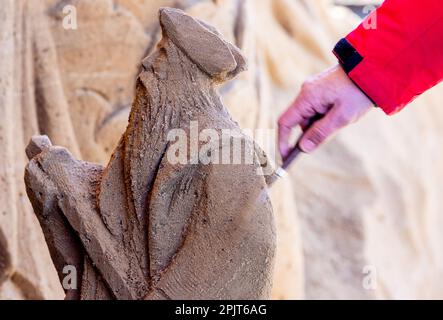 PRODUKTION - 03. April 2023, Mecklenburg-Vorpommern, Warnemünde: Ein Künstler aus Lettland arbeitet an einer großen Sandskulptur mit Neptun und anderen Unterwasserkreaturen. Sechs Künstler aus fünf Ländern kreieren die Figuren für die 13. Sand World aus 300 Tonnen Spezialsand direkt am Meereskanal in Warnemünde. Unter dem Motto „Metamorphose - Blown by the (Baltic) Wind“ werden bis zum 06. April 2023 verschiedene Motive rund um das Thema Meer geschaffen. Die Show wird bis zum 29. Oktober 2023 ausgestellt. Foto: Jens Büttner/dpa Stockfoto