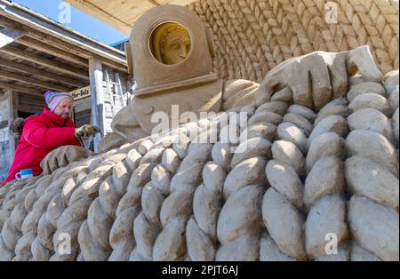 PRODUKTION - 03. April 2023, Mecklenburg-Vorpommern, Warnemünde: Sandkünstler Andrius Petkus aus Litauen arbeitet mit einem Taucher an einer großen Sandskulptur. Sechs Künstler aus fünf Ländern kreieren die Figuren für die 13. Sand World aus 300 Tonnen Spezialsand direkt am Meereskanal in Warnemünde. Unter dem Motto „Metamorphose - Blown by the (Baltic) Wind“ werden bis zum 06. April 2023 verschiedene Motive rund um das Thema Meer geschaffen. Die Show wird bis zum 29. Oktober 2023 ausgestellt. Foto: Jens Büttner/dpa Stockfoto