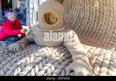 PRODUKTION - 03. April 2023, Mecklenburg-Vorpommern, Warnemünde: Sandkünstler Andrius Petkus aus Litauen arbeitet mit einem Taucher an einer großen Sandskulptur. Sechs Künstler aus fünf Ländern kreieren die Figuren für die 13. Sand World aus 300 Tonnen Spezialsand direkt am Meereskanal in Warnemünde. Unter dem Motto „Metamorphose - Blown by the (Baltic) Wind“ werden bis zum 06. April 2023 verschiedene Motive rund um das Thema Meer geschaffen. Die Show wird bis zum 29. Oktober 2023 ausgestellt. Foto: Jens Büttner/dpa Stockfoto