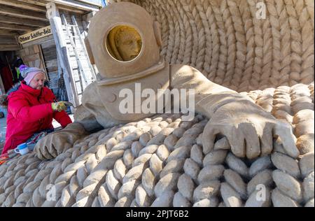 PRODUKTION - 03. April 2023, Mecklenburg-Vorpommern, Warnemünde: Sandkünstler Andrius Petkus aus Litauen arbeitet mit einem Taucher an einer großen Sandskulptur. Sechs Künstler aus fünf Ländern kreieren die Figuren für die 13. Sand World aus 300 Tonnen Spezialsand direkt am Meereskanal in Warnemünde. Unter dem Motto „Metamorphose - Blown by the (Baltic) Wind“ werden bis zum 06. April 2023 verschiedene Motive rund um das Thema Meer geschaffen. Die Show wird bis zum 29. Oktober 2023 ausgestellt. Foto: Jens Büttner/dpa Stockfoto