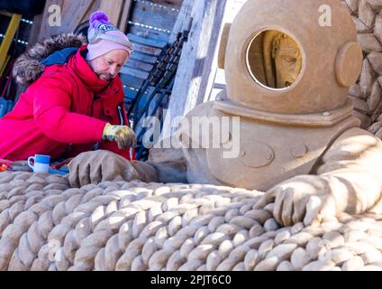 PRODUKTION - 03. April 2023, Mecklenburg-Vorpommern, Warnemünde: Sandkünstler Andrius Petkus aus Litauen arbeitet mit einem Taucher an einer großen Sandskulptur. Sechs Künstler aus fünf Ländern kreieren die Figuren für die 13. Sand World aus 300 Tonnen Spezialsand direkt am Meereskanal in Warnemünde. Unter dem Motto „Metamorphose - Blown by the (Baltic) Wind“ werden bis zum 06. April 2023 verschiedene Motive rund um das Thema Meer geschaffen. Die Show wird bis zum 29. Oktober 2023 ausgestellt. Foto: Jens Büttner/dpa Stockfoto