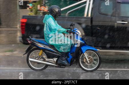 Ein Mann in einem Regenmantel fährt bei starkem Regen auf der Straße mit dem Motorrad, Thailand Stockfoto