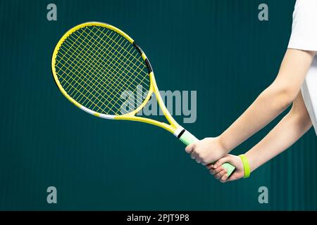Tennisschläger in den Händen eines Mädchens aus der Nähe - auf dunkelgrünem Hintergrund. Das Tennisspiel Stockfoto