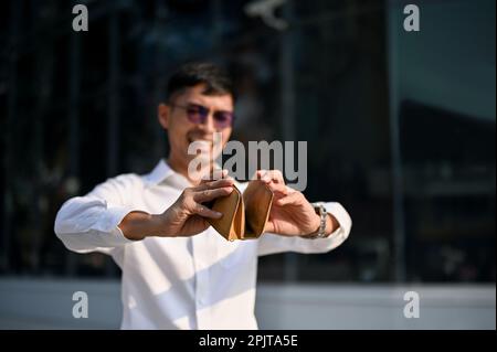 Gestresst und pleite, ein asiatischer Geschäftsmann, der seine leere Brieftasche in der Stadt öffnet. Bankrott, Finanzproblem, Misserfolg Stockfoto