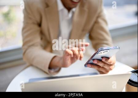 Nahaufnahme eines asiatischen Geschäftsmanns der Jahrtausendwende, der sein Smartphone benutzt, während er in einem Café sitzt. SMS, Chat, soziale Medien. Stockfoto